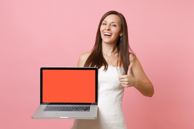 Laughing woman in white dress showing thumb up, hold laptop pc computer with blank black empty screen