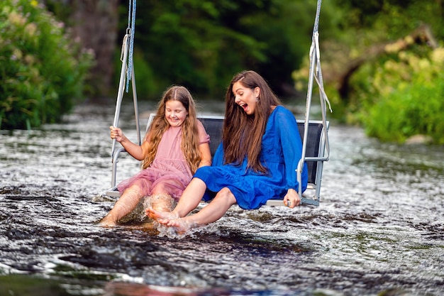 laughing woman and a young girl swing over a fastflowing river splashing the water with their feet