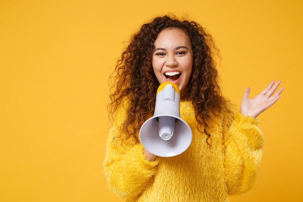 Photo laughing young african american girl in fur sweater posing isolated on yellow orange wall background studio portrait. people lifestyle concept. mock up copy space. scream in megaphone spreading hands.