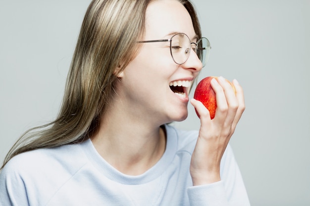 Фото Смеется молодая девушка ест яблоко. крупный план. здоровое питание и витамины.