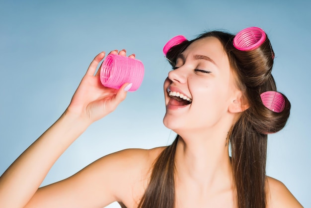 A laughing young girl makes a fashionable hairstyle with a large pink curler