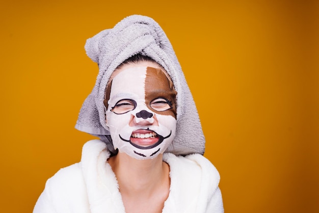 A laughing young girl with a towel on her head wants to be beautiful on her face a moisturizing mask with a dog39s face