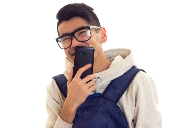 Laughing young man in white hoody with black glasses and blue backpack talking on the smartphone