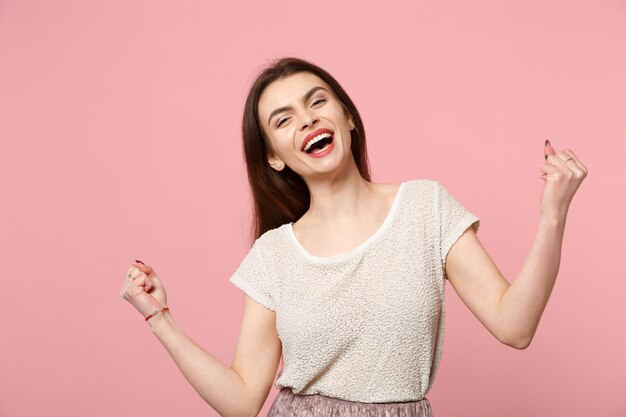 Laughing young woman in casual light clothes posing isolated on pastel pink background, studio portrait. People sincere emotions lifestyle concept. Mock up copy space. Clenching fists like winner.