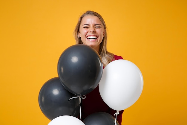 Laughing young woman girl in casual clothes posing isolated on yellow orange background. Birthday holiday party, people emotions concept. Mock up copy space. Celebrating holding colorful air balloons.