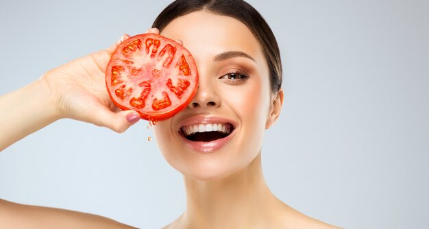 Photo laughing young woman is holding red and juicy tomato in the hands with toothy smile and shiny facial expression