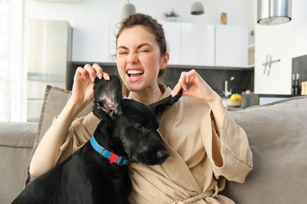 写真 ソファで犬と遊ぶ若い女性を笑いながらペットの長い耳を見せて微笑むかわいい女の子