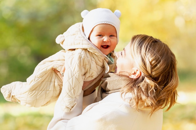 Photo laughing young woman with toddler cuddling in an autumn park on a sunny day. love and tenderness. close-up.