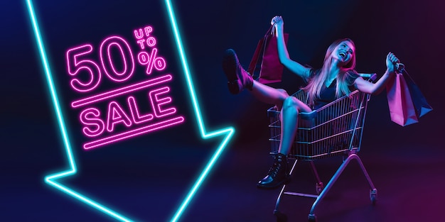 Laughting, shopping. Portrait of young woman in neon on dark studio backgound. Human emotions, black friday, cyber monday, purchases, sales, finance concept. Copyspace. Seamless post for instagram.