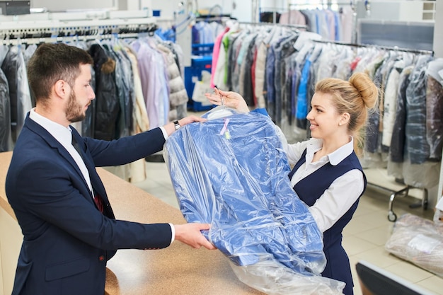 Laundry worker girl man gives the customer clean clothes in dry cleaners