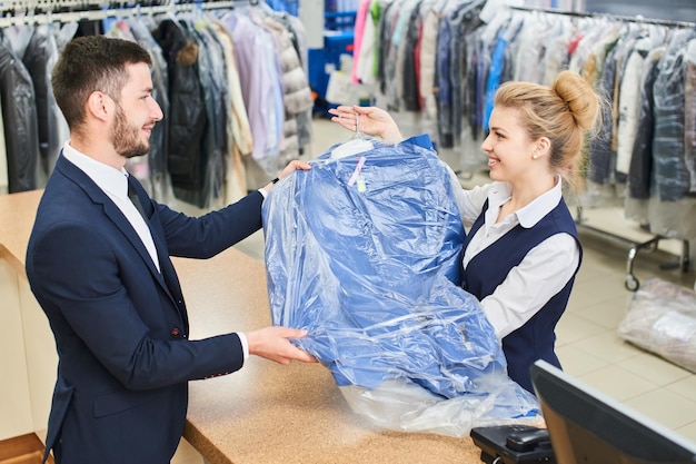 Laundry worker girl man gives the customer clean clothes in dry cleaners