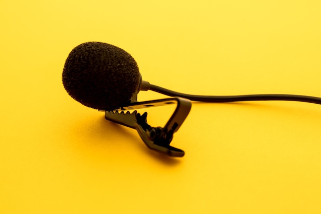 Lavalier or lapel microphone on a yellow surface, very\
close-up. the details of the grip clip or bra and the sponge\
against the wind are visible.