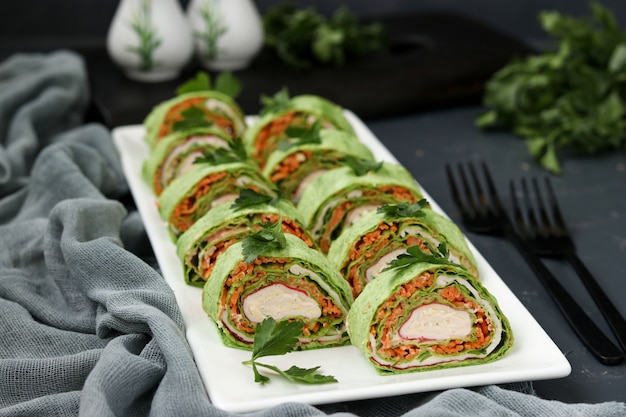 Lavash roll with crab sticks, spinach, parsley and carrots in Korean style on a plate against a dark 