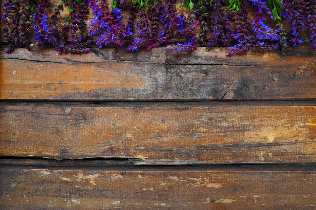 Lavendel en salie bloemen op een houten tafel close-up Horizontale planken van donker oud hout met paarse en blauwe bloemen en bladeren rond de randen Stilleven en plat leggen Gratis kopieerruimte voor tekst