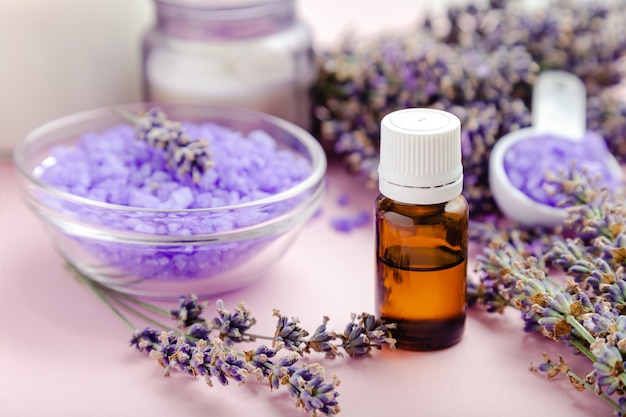 Contagocce di bottiglia di vetro di olio essenziale di lavanda con sale marino viola prodotto da bagno su sfondo di colore rosa. fiori di lavanda freschi. trattamento aromaterapico. cosmetici per la cura della pelle spa, erbe aromatiche lavanda