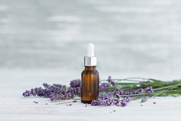 Lavender herbal oil and lavender flowers on grey wooden background.