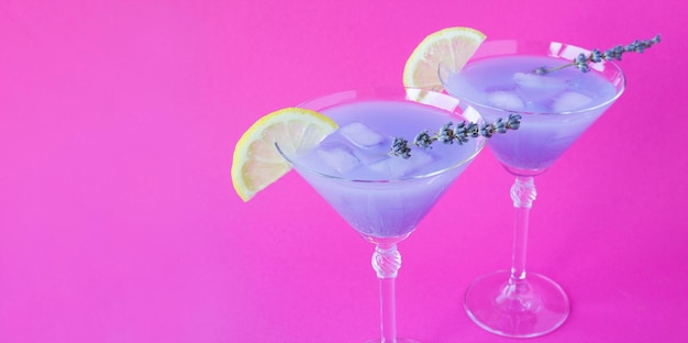 Lavender lemonade with lemon and ice in martini glasses on the bright pink background Copy space Closeup