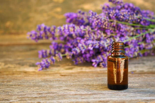 Lavender oil in different bottles and lavender flowers in the back on wooden background.