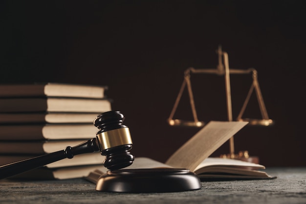 Концепция закона - открытая книга закона с деревянным молотком судей на столе в зале суда или в офисе правоохранительных органов на черном фоне.