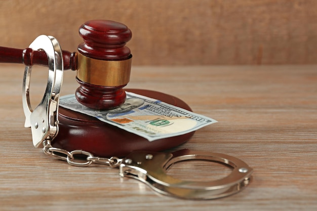 Law gavel with dollars and handcuffs on wooden table background closeup