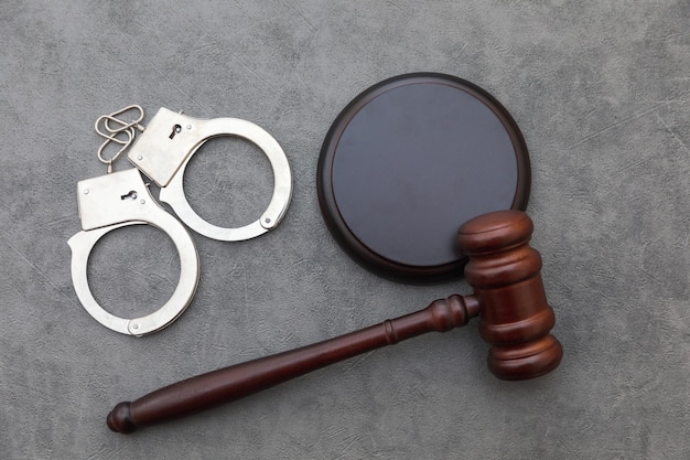 Фото Юридическая тема судебное разбирательство на заседании судьи молотком наручники на сером столе в офисе адвоката или в суде