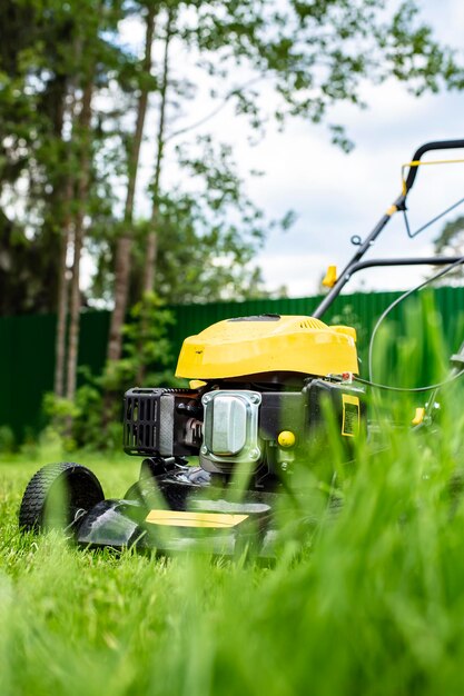 Photo lawn mower on green grass against a background of trees and a fence in the yard