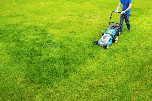 Photo a lawn mower is cutting green grass the gardener with a lawn mower is working in the backyard