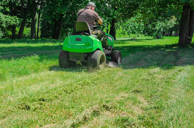 Photo lawn mower rides on the lawn and mows the grass mowing the lawn in the park