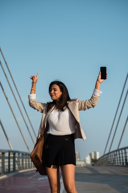 A lawyer celebrates victory on the street with her cell phone and briefcase in the middle of a bridge Copy space