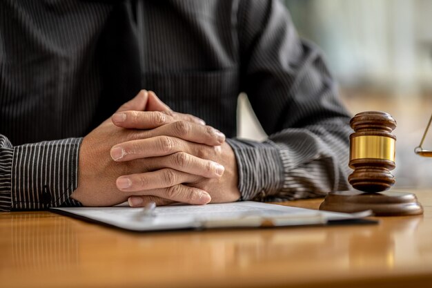 Foto un avvocato si siede nel suo ufficio su un tavolo con un piccolo martello per battere la scrivania del giudice in tribunale e gli avvocati della bilancia della giustizia stanno redigendo un contratto che il cliente può utilizzare con l'imputato per firmare