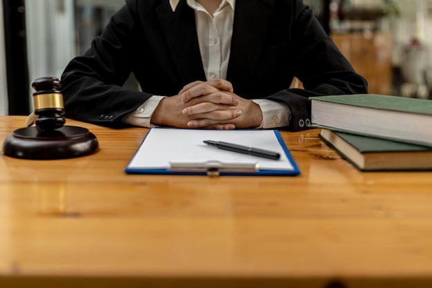 A lawyer sits in his office, on a table with a small hammer to beat the judges desk in court. and justice scales, lawyers are drafting a contract for the client to use with the defendant to sign.