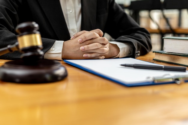 A lawyer sits in his office, on a table with a small hammer to beat the judges desk in court. and justice scales, lawyers are drafting a contract for the client to use with the defendant to sign.