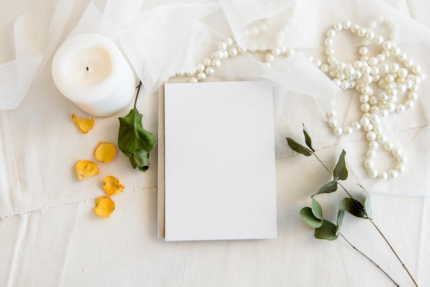 Lay-outscène van een briefpapierlay-out Een lege verticale wenskaart een parelsnoer en gedroogde bloemen geïsoleerd op een witte tafelachtergrond Bovenaanzicht leeg voor uitnodiging