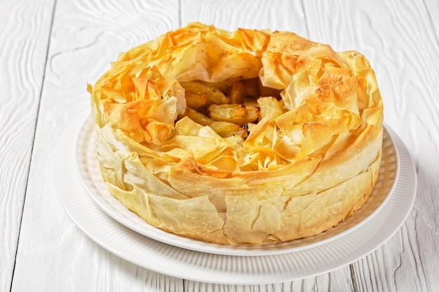 Фото Слоеный яблочный пирог с phyllo crust на белом блюде на белом деревянном столе, горизонтальный вид сверху, крупный план