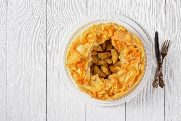 Layered Apple Pie With Phyllo Crust on a white platter on a white wooden table, horizontal view from above, flat lay, free space