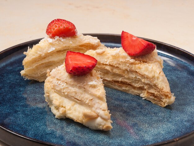 Layered Napoleon cake decorated with strawberries on a blue plate in a restaurant