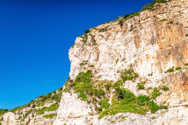 Layered rocky cliffs with plants near shore of Corfu island