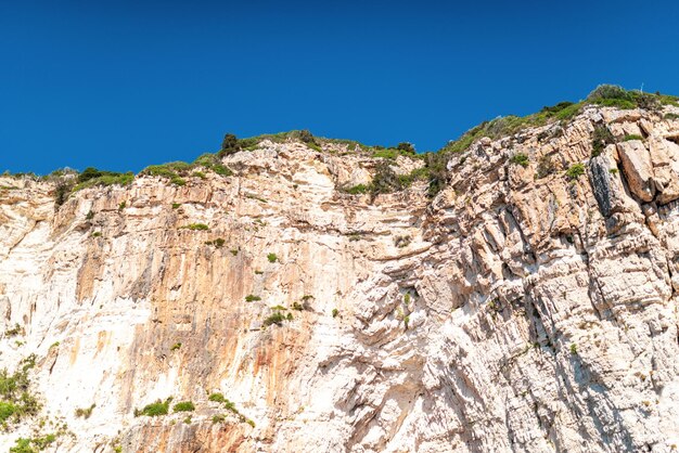 Layered rocky cliffs with plants near shore of Corfu island