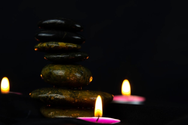 Layers of stones are on dark background two rounded candles with white towel use for massage