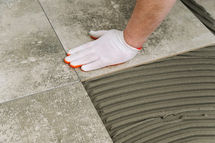 Laying Ceramic Tiles. Worker placing ceramic floor tile in position over adhesive.