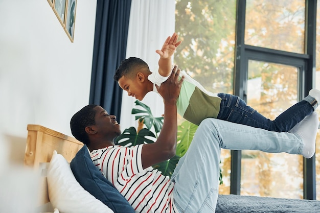 Laying down on the bed and having fun African american father with his young son at home