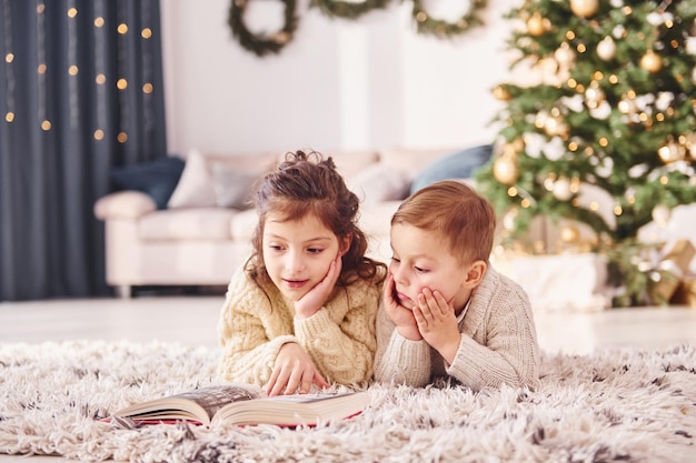 Photo laying down on the ground little brother and sister is at christmas decorated room together