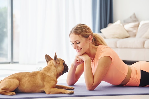 マットに寝そべるパグ犬を連れた女性が昼間家にいる