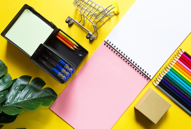 Layout of multicolored stationery on a yellow background spiral notebook, colored pencils,