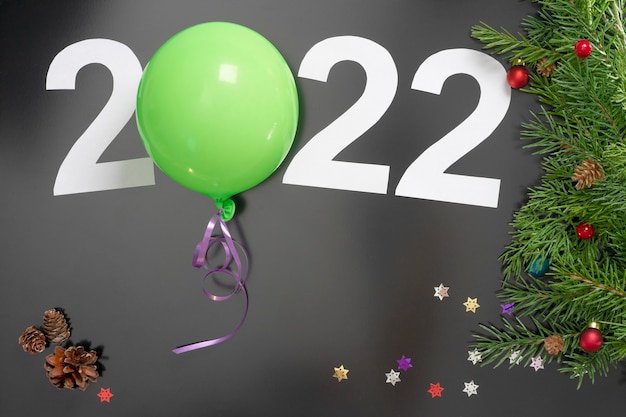 Layout on the theme of the New Year 2022 with numbers, a ball, toys and Christmas tree branches against a dark background.