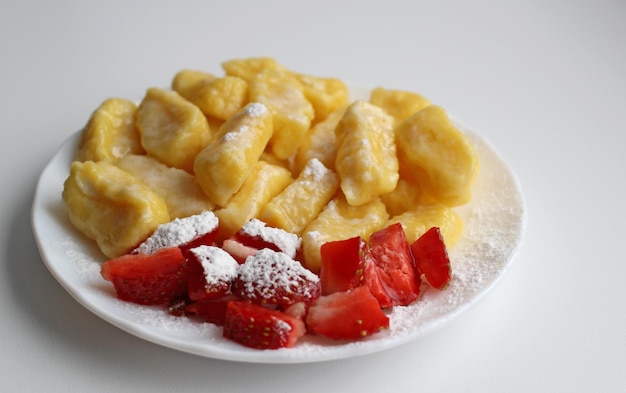 Lazy dumplings with fresh strawberries and powdered sugar on a white saucer