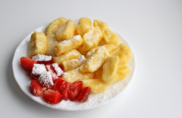 Lazy dumplings with fresh strawberries and powdered sugar on a white saucer