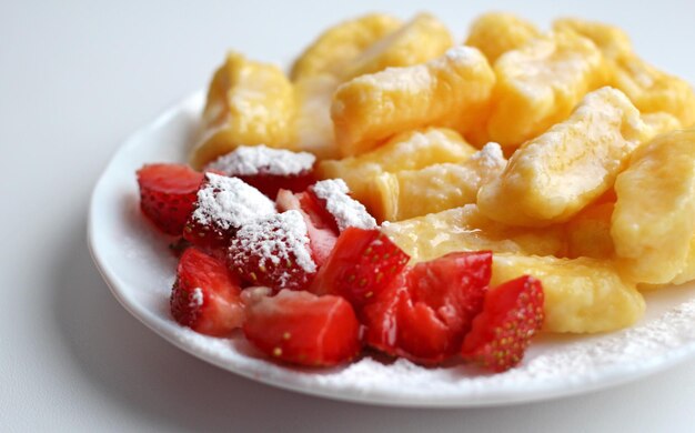 Lazy dumplings with fresh strawberries and powdered sugar on a white saucer