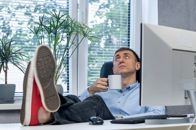 Photo lazy employee in office put his feet on desk and drinks coffee. man in procrastination. lunch time.