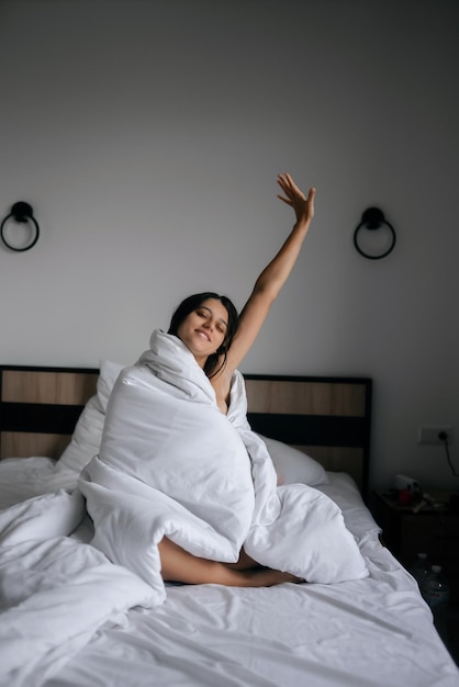 Lazy female wrapped in soft blanket sitting in cozy bed